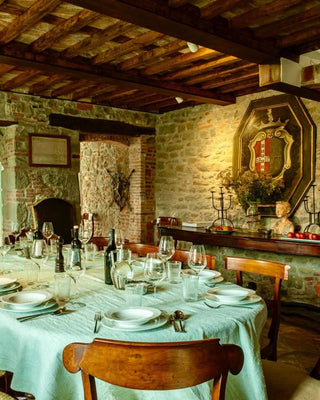 Sala da pranzo di Villa Di Valgiano con tavola apparecchiata, pareti in pietra e soffitto con travi in legno.
