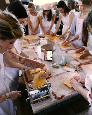 Preparazione della pasta fresca durante una lezione di cucina, con sfoglia tirata a macchina e impasto lavorato a mano.
