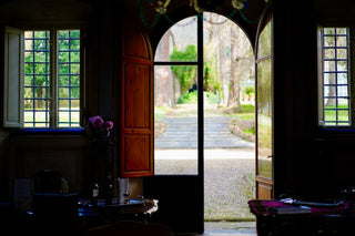 Portone ad arco di Villa Di Valgiano aperto sul giardino, con un viale alberato e gradini in pietra.