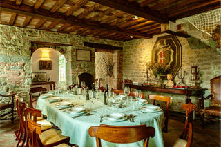 Sala da pranzo di Villa Di Valgiano con tavola apparecchiata, pareti in pietra e soffitto con travi in legno.