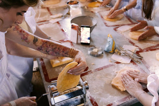 Preparazione della pasta fresca durante una lezione di cucina, con sfoglia tirata a macchina e impasto lavorato a mano.
