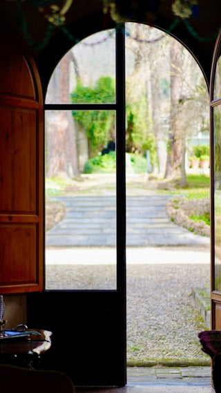 Portone ad arco di Villa Di Valgiano aperto sul giardino, con un viale alberato e gradini in pietra.