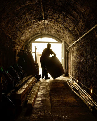 Interno della cantina storica della Tenuta di Valgiano, con volta in mattoni e una persona che movimenta una botte.