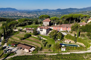 Vista aerea della Tenuta di Valgiano, con edifici storici, giardini e piscina, affacciata sulla piana di Lucca.
