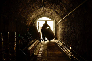 Interno della cantina storica della Tenuta di Valgiano, con volta in mattoni e una persona che movimenta una botte.