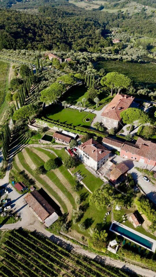 Vista aerea della Tenuta di Valgiano, con edifici storici, giardini e piscina, affacciata sulla piana di Lucca.