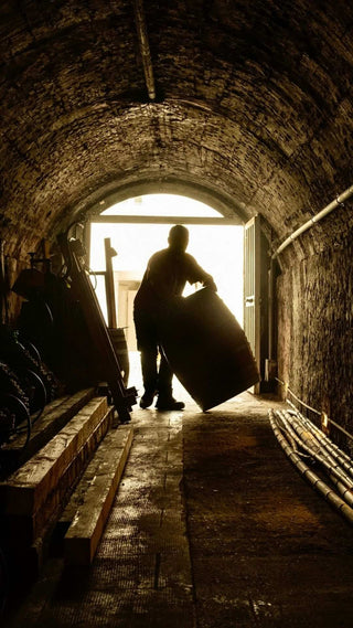 Interno della cantina storica della Tenuta di Valgiano, con volta in mattoni e una persona che movimenta una botte.