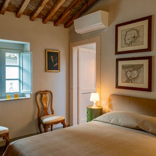 Camera matrimoniale con testiera imbottita, stampe incorniciate sopra il letto e finestra con imposte azzurre.