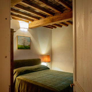 Camera matrimoniale con copriletto verde, lampada sul comodino e travi in legno, vista dalla porta aperta.