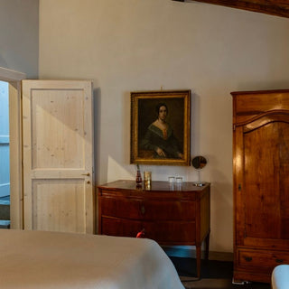 Camera matrimoniale con comò e armadio in legno, ritratto alla parete e porta chiara aperta.