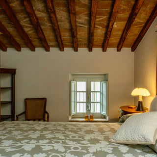 Camera matrimoniale con copriletto a motivi floreali, poltrona e soffitto con travi in legno a vista.