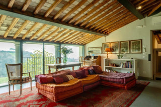 Soggiorno di Villa Di Valgiano con divani colorati, tappeto e soffitto in legno, affacciato sulle colline
