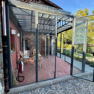 Vista esterna della veranda della dependance, con struttura in vetro e metallo e porta aperta sul giardino.