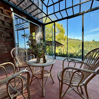Veranda vetrata della dependance di Villa Di Valgiano con poltrone in vimini, tavolino e vista sulle colline.