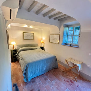 Camera matrimoniale della dependance con letto sotto un arco, travi chiare a vista e finestra sul giardino.