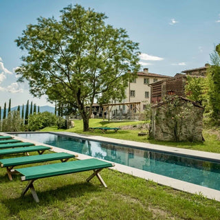 Piscina privata di Villa Di Valgiano con lettini verdi sul prato, un grande albero e la villa sullo sfondo