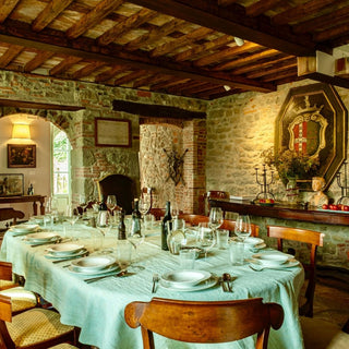 Sala da pranzo di Villa Di Valgiano con tavola apparecchiata, pareti in pietra e soffitto con travi in legno.